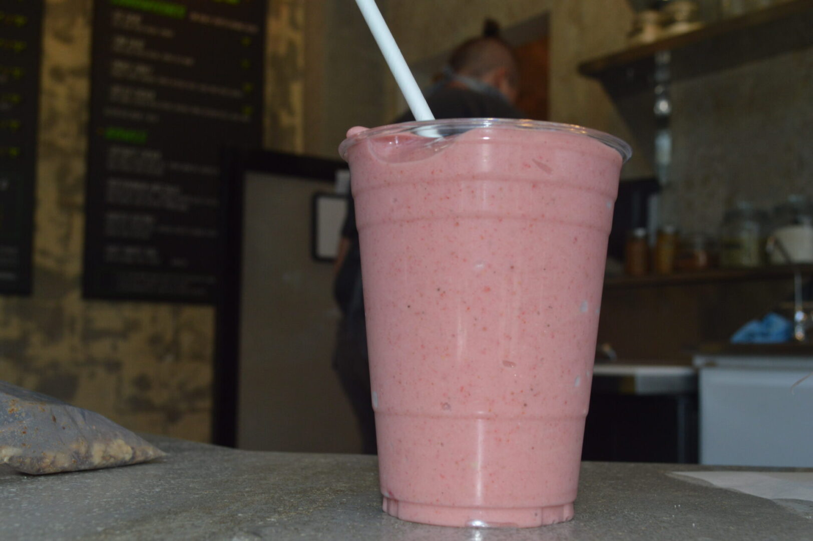 A pink smoothie in a plastic cup with a straw.