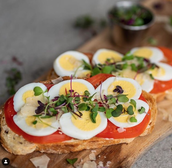 A sandwich with eggs, tomatoes and herbs on it.
